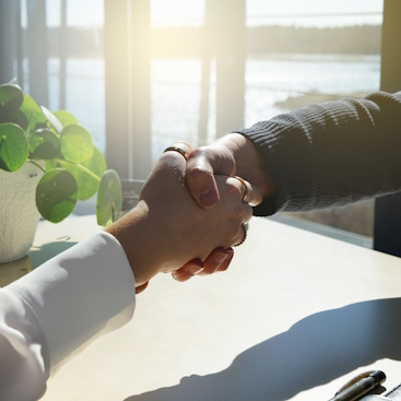 Zwei Personen, die sich die Hand geben. Zwei Personen, die sich über einem Tisch die Hand geben.